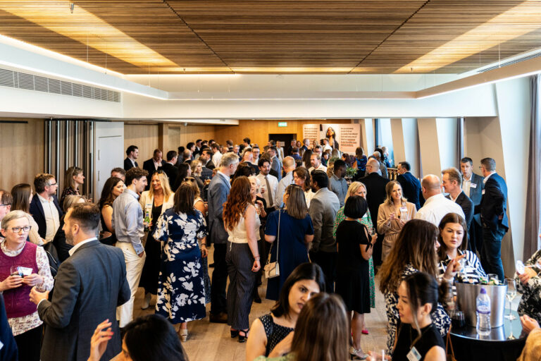 A bustling well lit breakout room full of people mingling together.