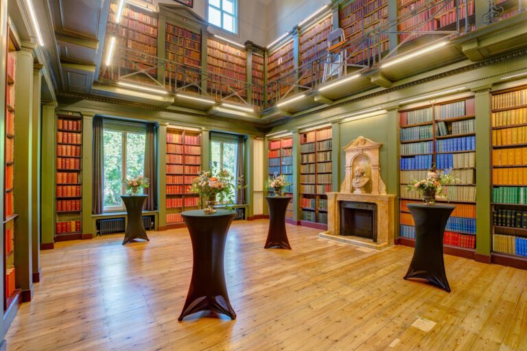 The Library room set up with four small but tall tables covered in black tablecloths, each featuring a vase of flowers.