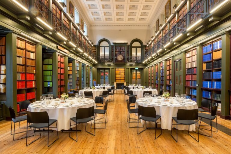 The Lumley Library room set up in a reception style seating arrangement. There are six tables visible, all of which are covered by white tablecloths and laid with cutlery.